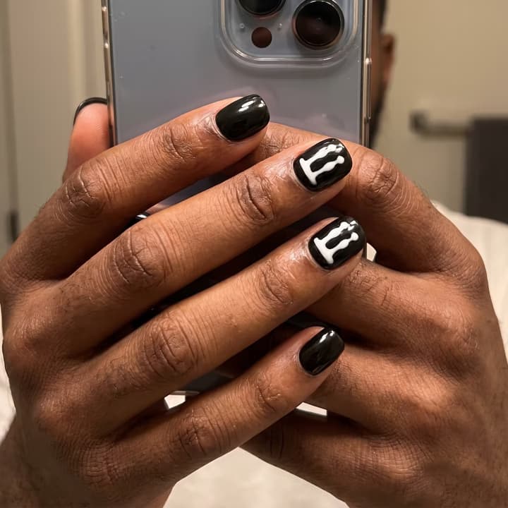 Deep skin-tone hand with short glossy black press-on nails and white drip art, mirror selfie