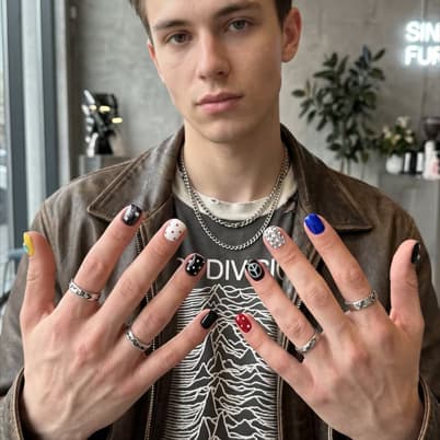 Hands showing a mismatched multi-color press-on set — blue, red, yellow and dotted nails
