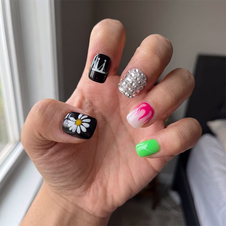 Light-medium skin hand with a playful mixed press-on set — daisy, crown and gem nails