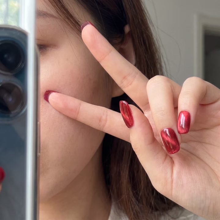 Fair skin hand throwing a peace sign with glossy cherry-red press-on nails