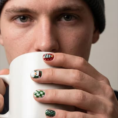 Hands around a mug showing holiday press-on nails โ Santa, snowman and green check